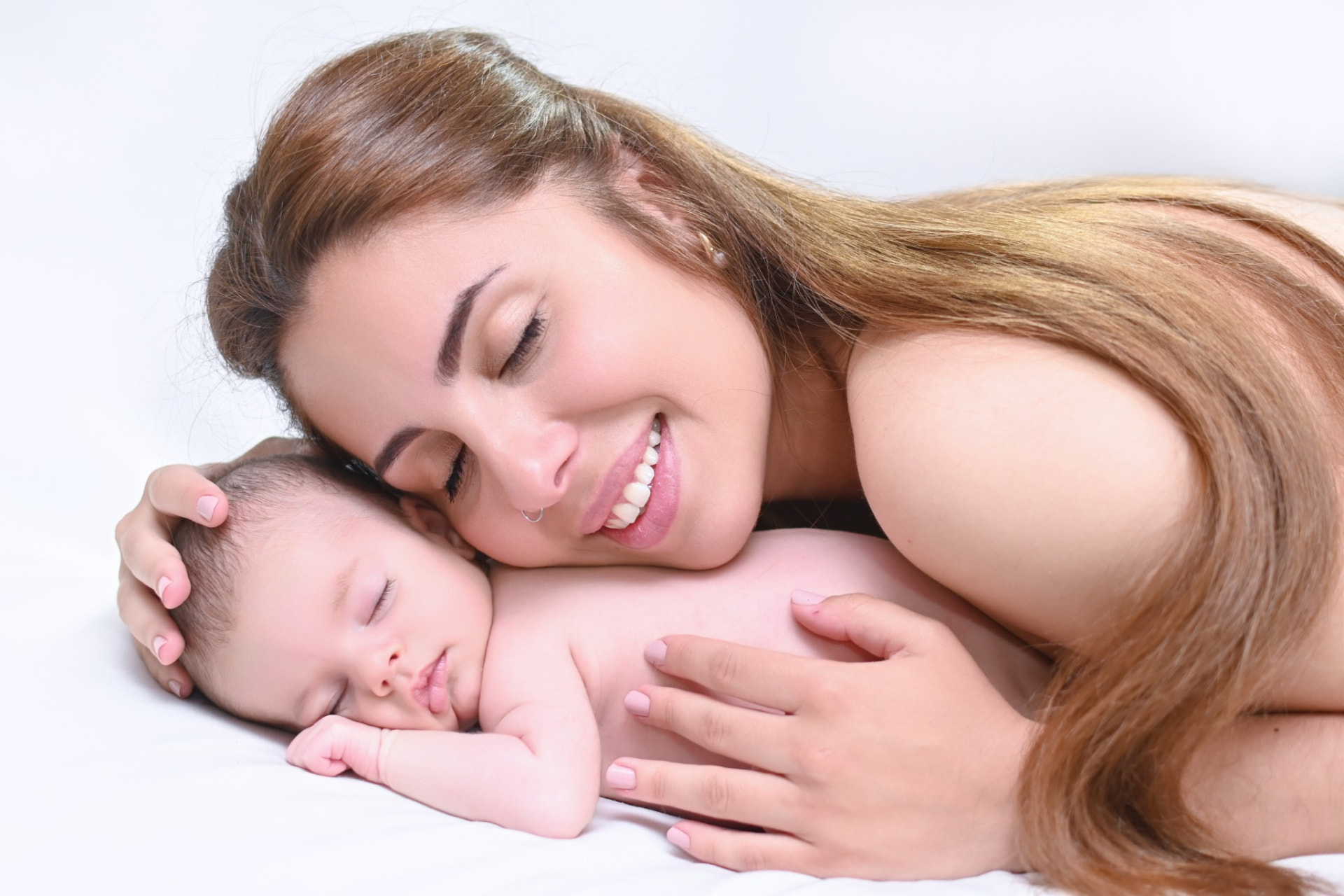 Madre sonriendo con la mejilla apoyada en su bebé recién nacido dormido durante una sesión newborn en Fuenlabrada