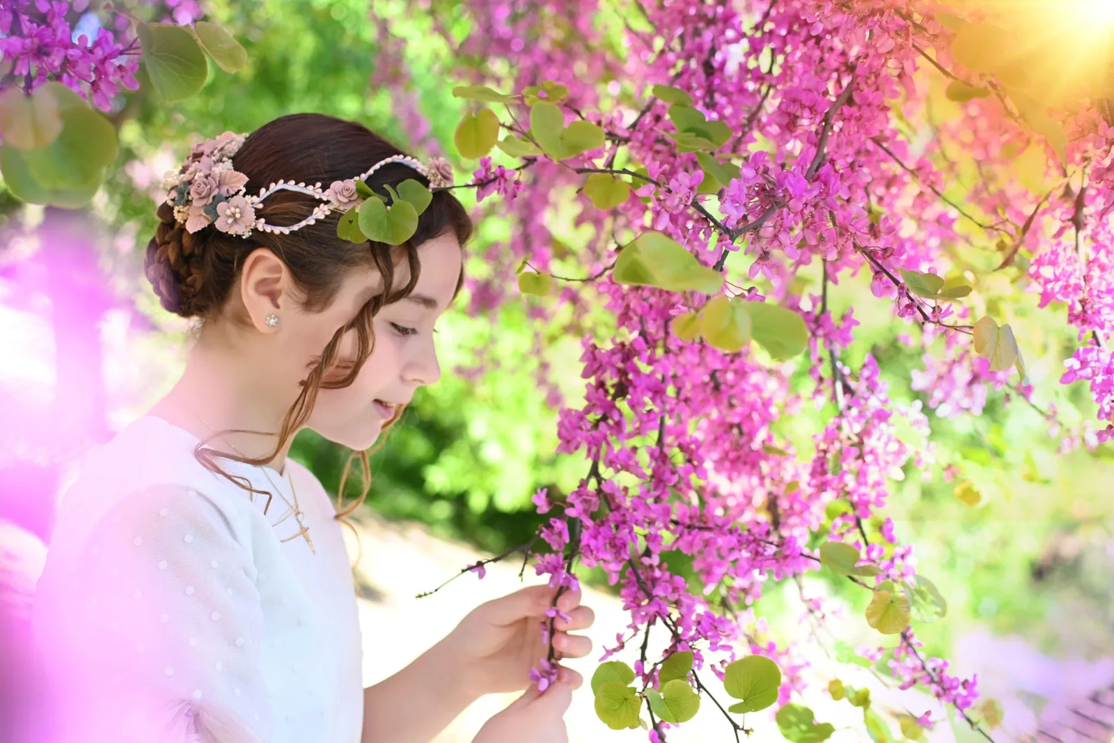 Niña de Comunión con tocado de flores mirando las ramas de un árbol en flor rosa