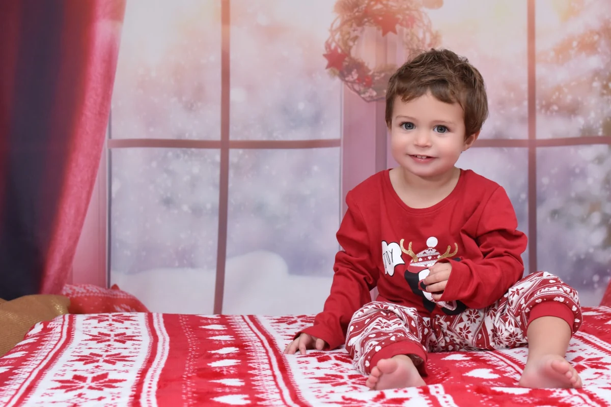 Niño pequeño con pijama rojo sentado y mirando a cámara, campaña de Navidad 2020