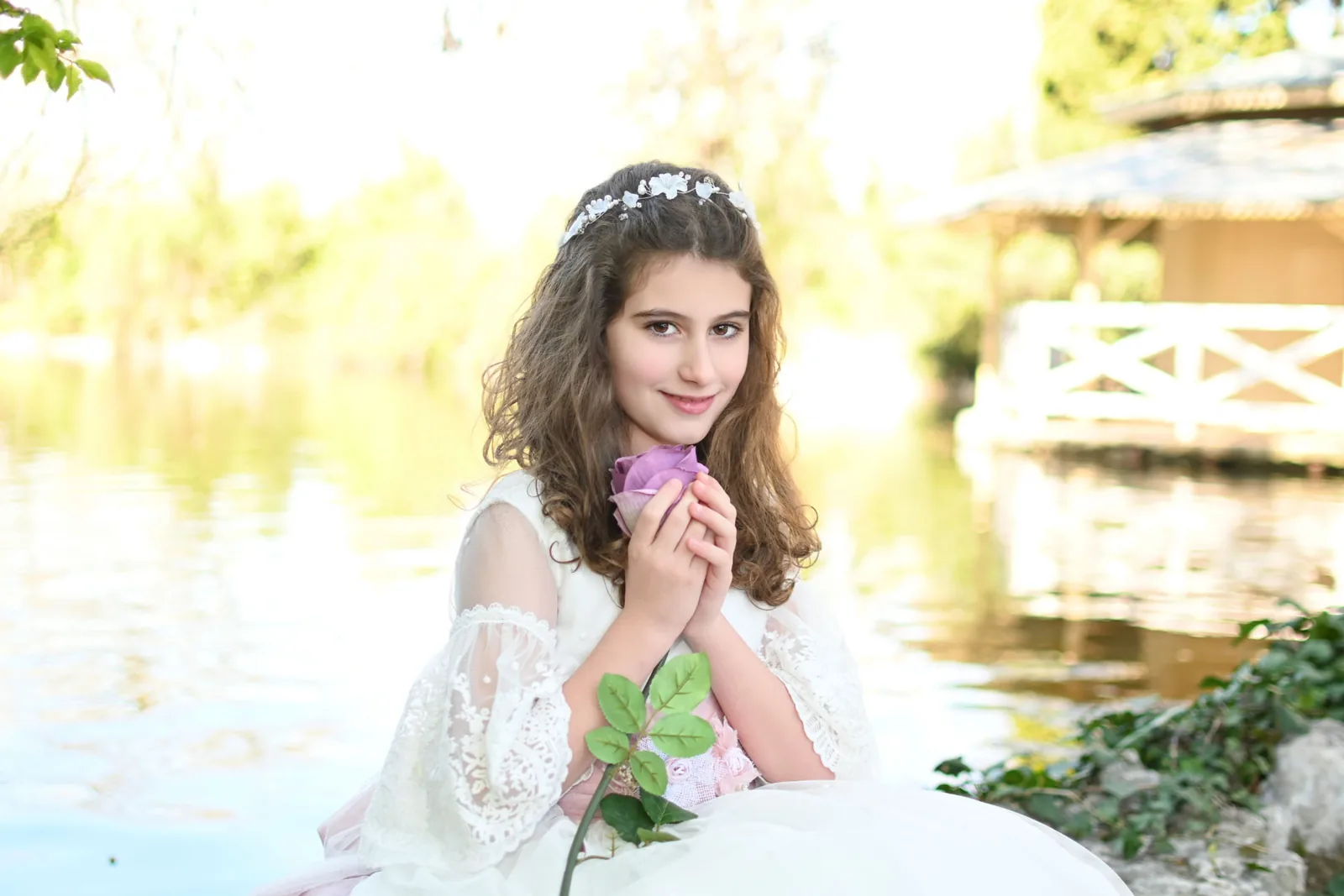Retrato de niña de Comunión con una rosa malva sentada junto al lago