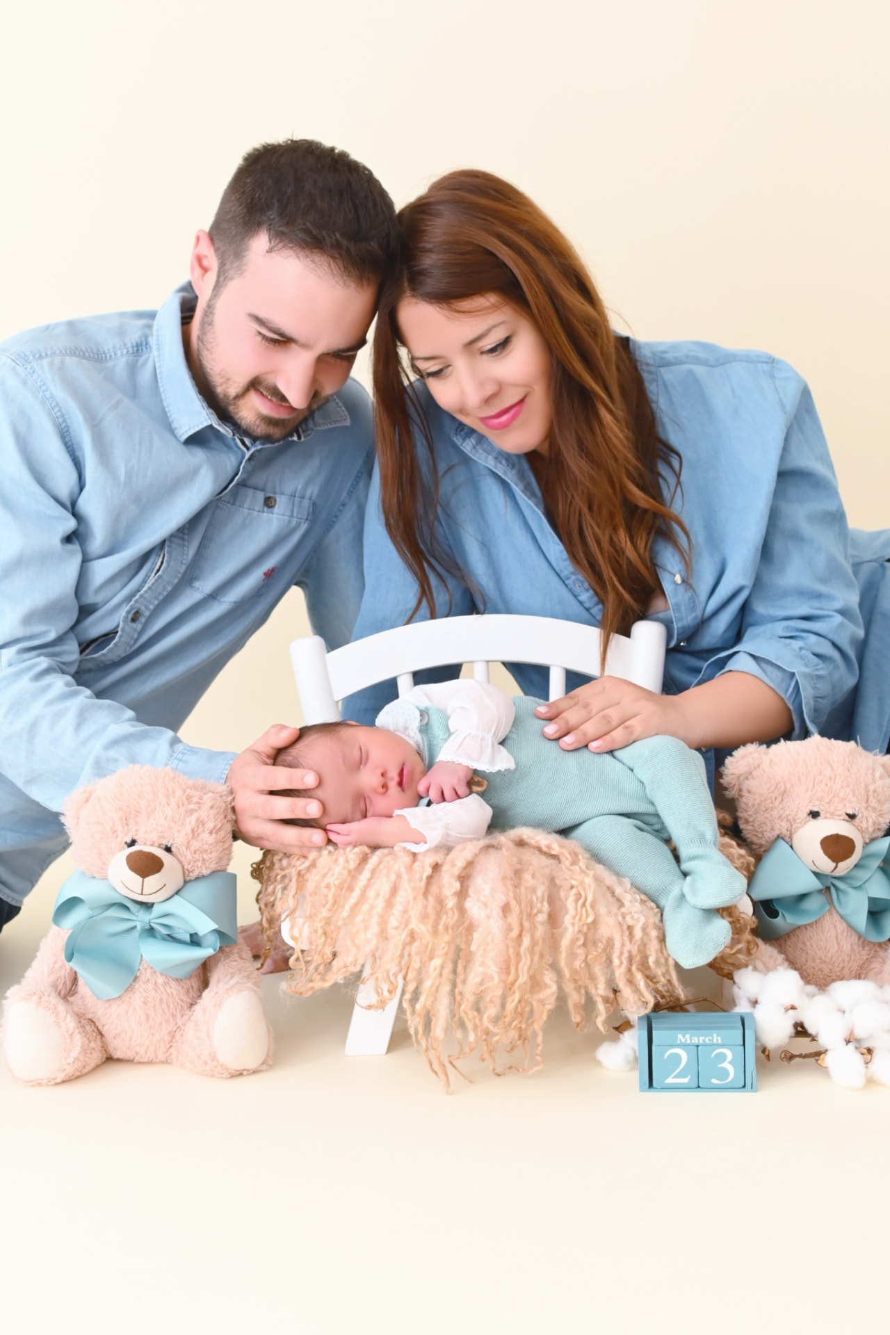 Pareja de padres mirando con ternura a su bebé recién nacido acompañado de dos ositos de peluche
