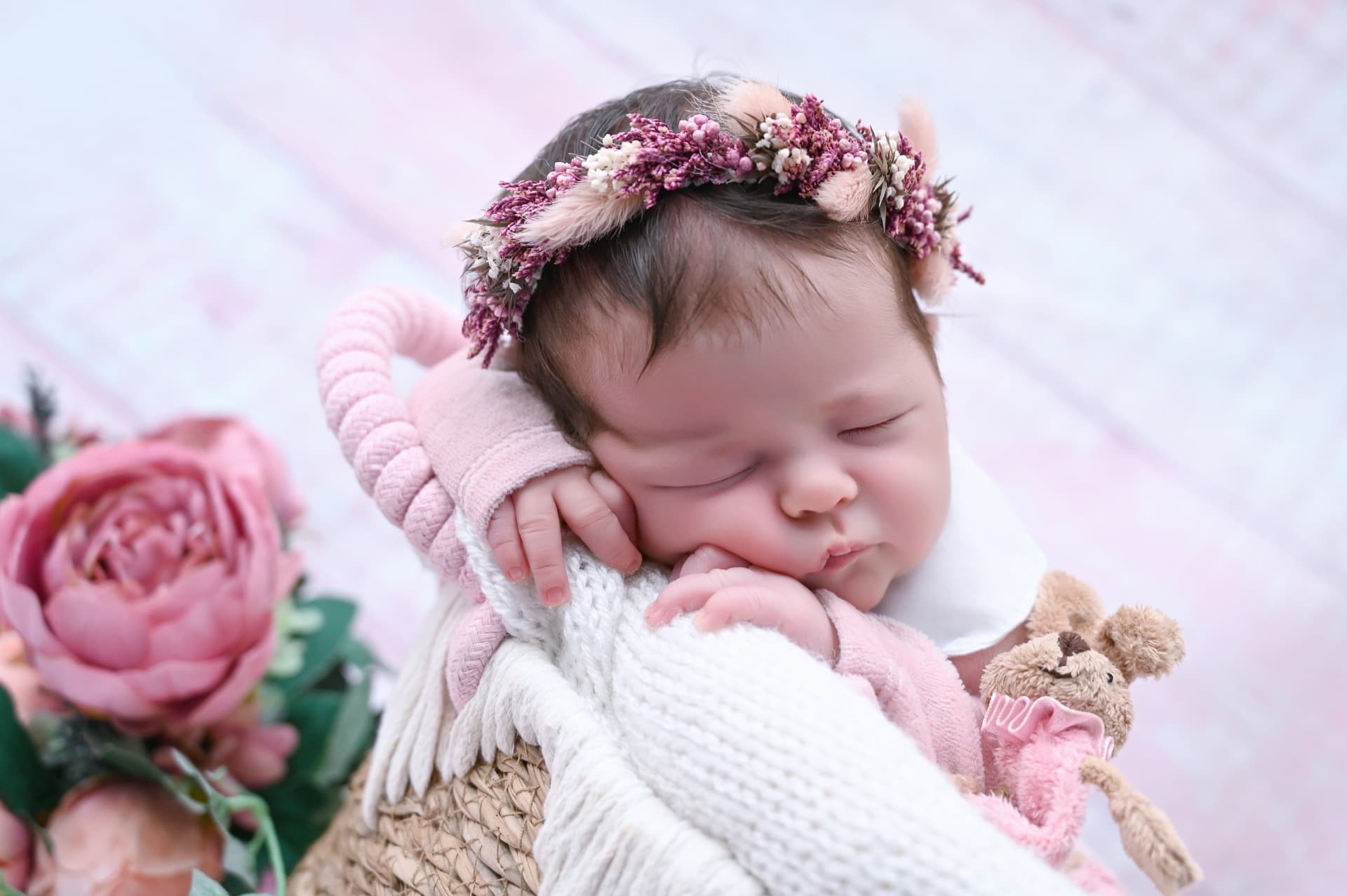 Bebé recién nacido dormido en una cesta con flores secas durante el posado