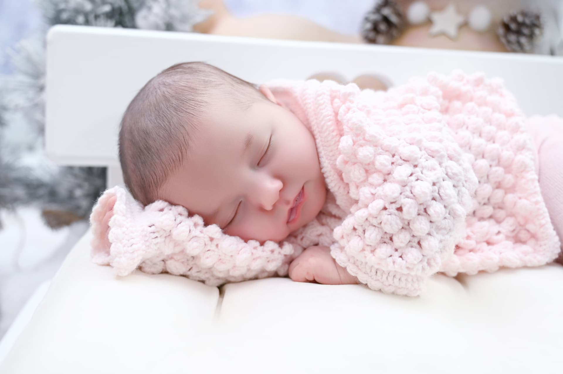 Bebé recién nacido dormido y envuelto en una manta rosa sobre un decorado navideño claro