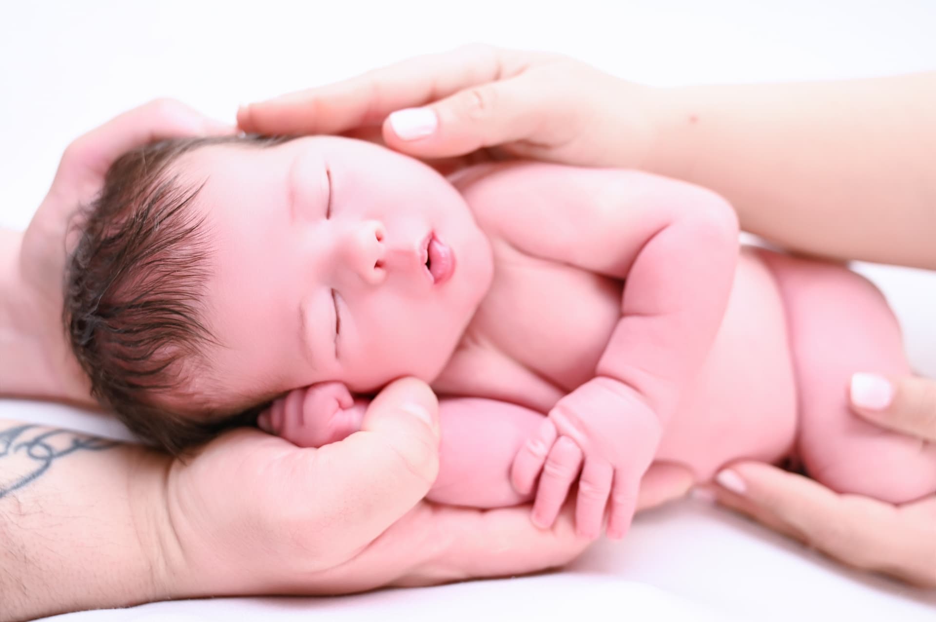 Bebé recién nacido dormido y desnudo entre las manos de sus padres