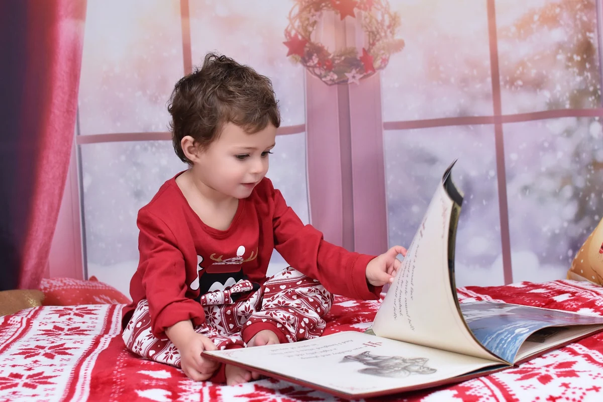 Niño con pijama rojo pasando las páginas de un libro, campaña de Navidad 2020