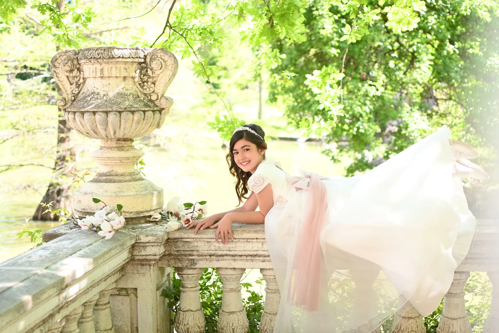 Niña de Primera Comunión con vestido de tul apoyada en una balaustrada de piedra con magnolias junto al lago