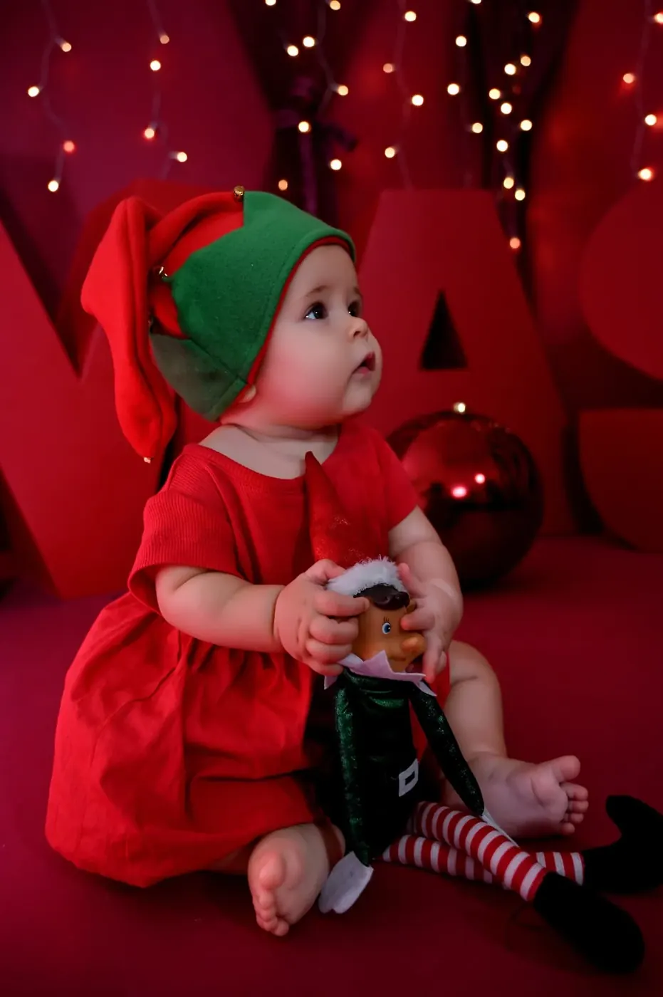 Bebé vestido de elfo con un teléfono en el decorado rojo de Navidad