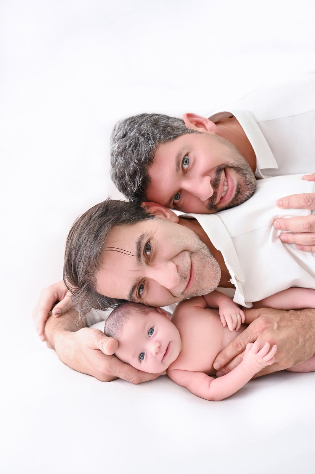 Dos padres tumbados abrazando a su bebé recién nacido en una sesión newborn en estudio