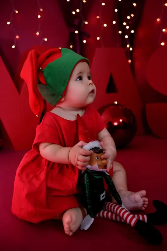 Bebé vestido de elfo con un teléfono en el decorado rojo de Navidad del estudio de Fuenlabrada