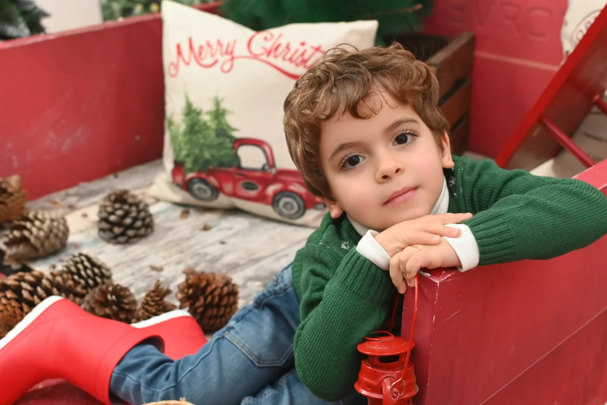 Niño recostado junto a piñas y un farol rojo en la campaña de Navidad 2021