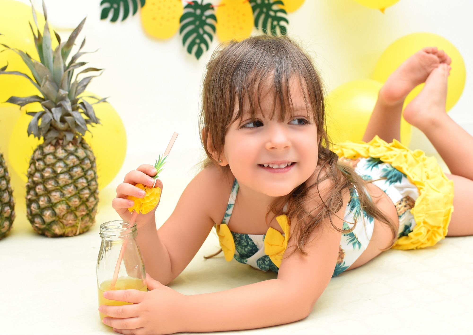 Niña sonriendo entre piñas y globos amarillos en una sesión de cumpleaños tropical