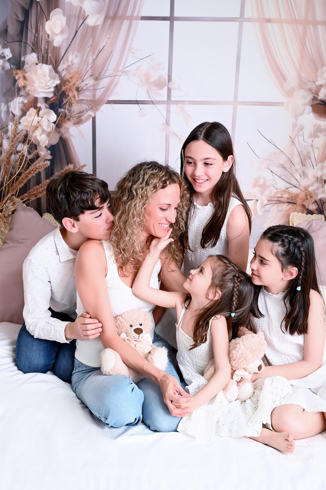 Madre rodeada de sus cuatro hijos, abrazados y riendo sobre la cama del estudio