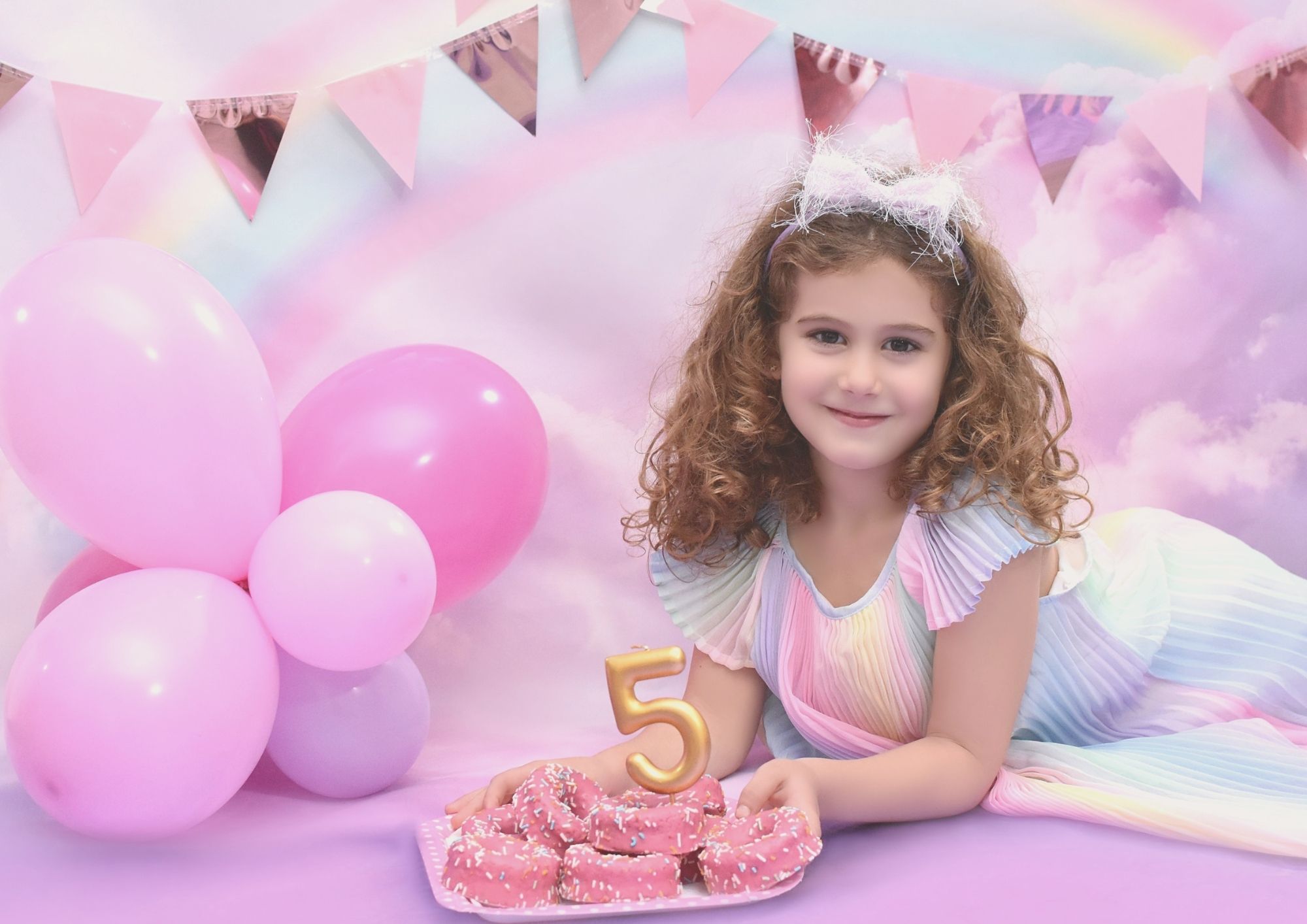 Niña de cinco años con donuts y vela en un decorado pastel durante su sesión de cumpleaños