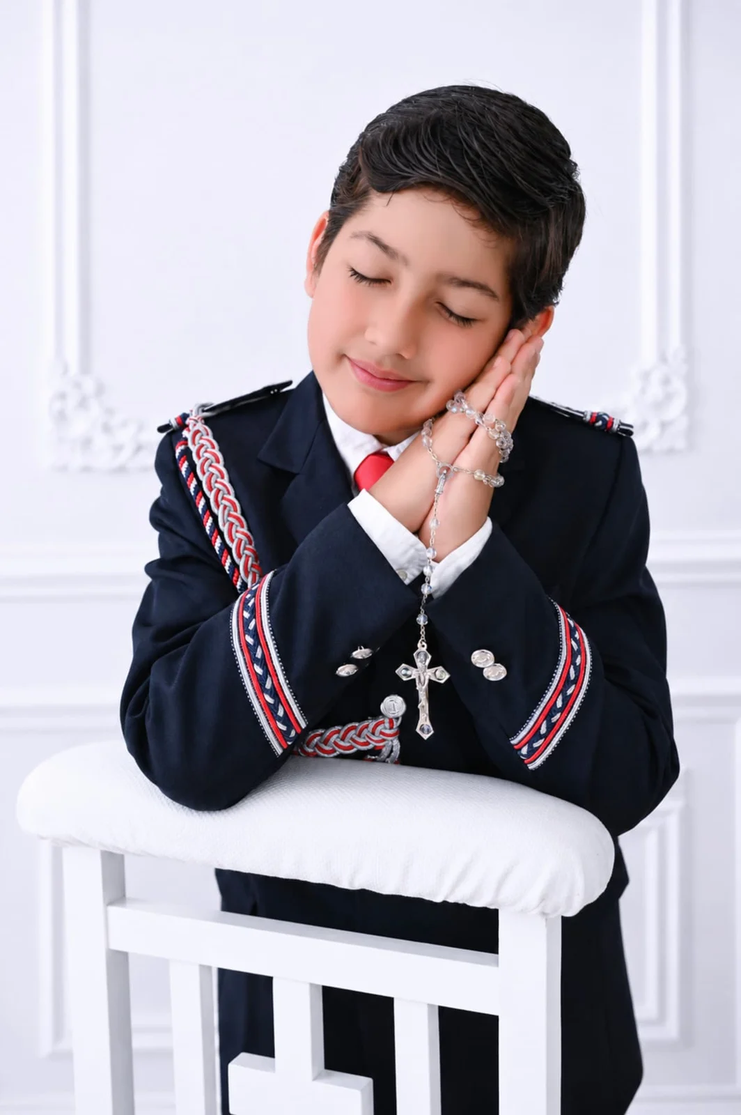 Retrato de niño durante una sesión de Comunión en estudio, con las manos juntas y un rosario