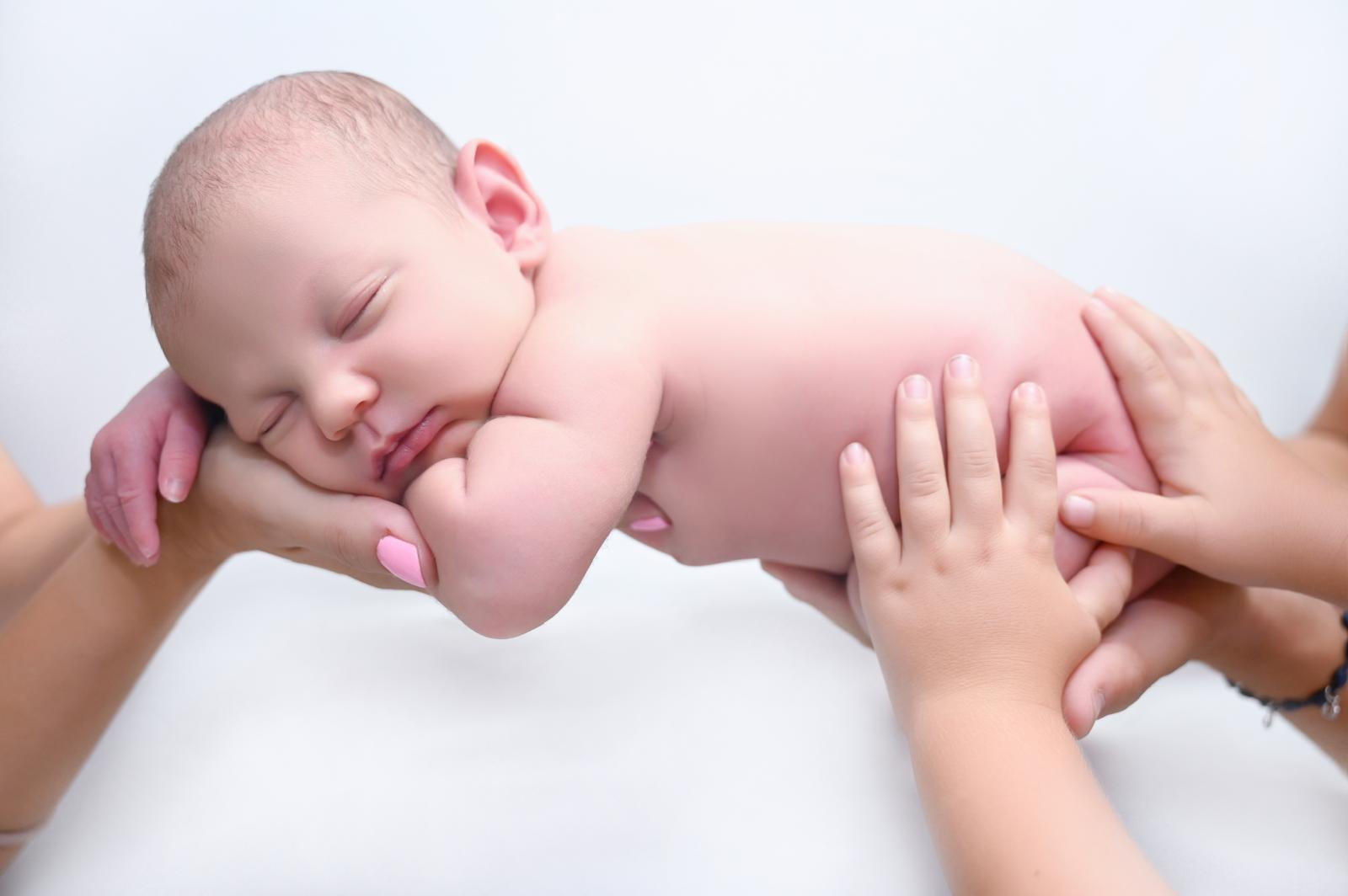 Bebé recién nacido sostenido entre las manos de sus padres sobre fondo blanco