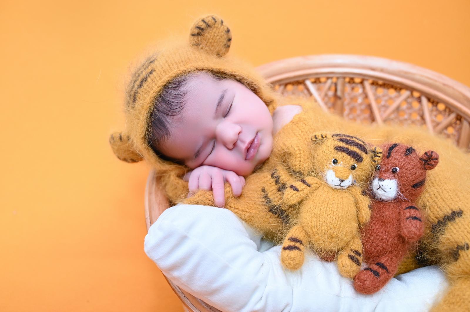 Bebé recién nacido dormido con gorrito de lana junto a sus ositos de peluche