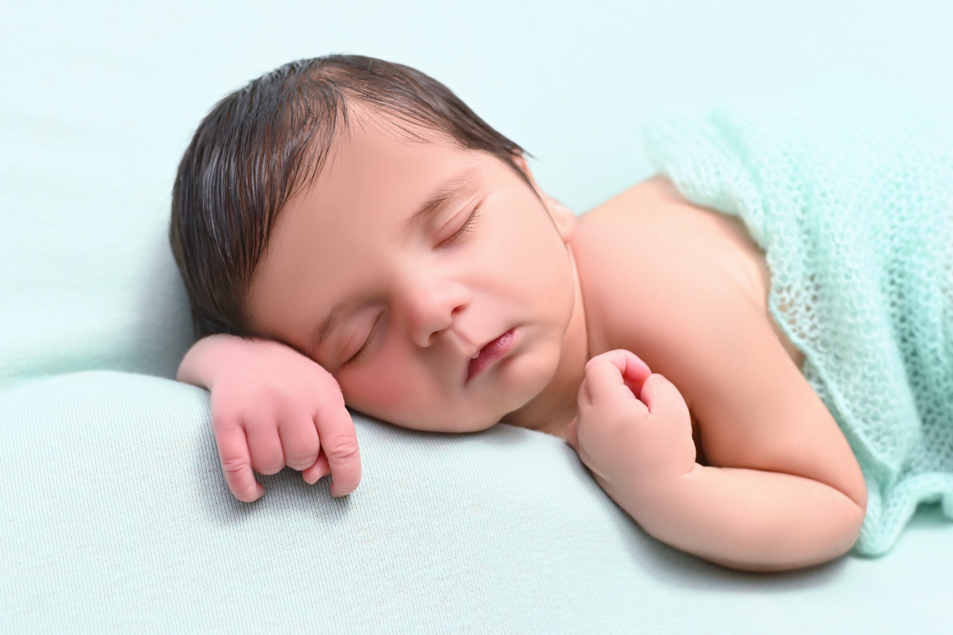 Recién nacido dormido sobre una manta verde agua en una sesión de fotos newborn en estudio