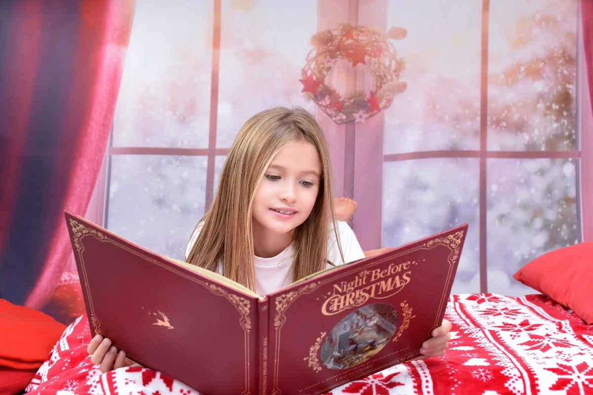 Niña leyendo un libro navideño sobre una cama con decoración roja y blanca, campaña 2020