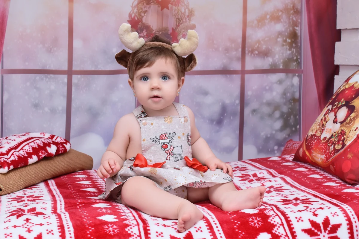 Bebé sentada con diadema de reno sobre una manta roja y blanca, campaña de Navidad 2020