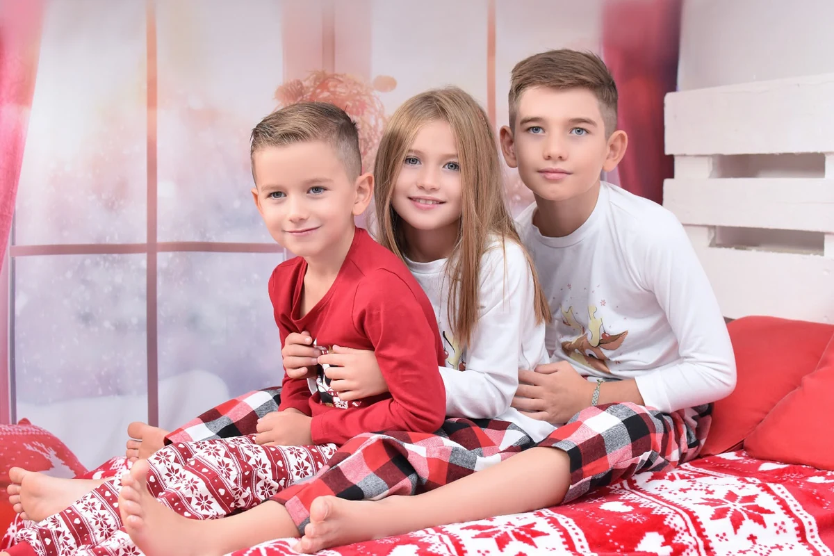 Tres niños en pijama sentados sobre una cama con decoración navideña, campaña 2020