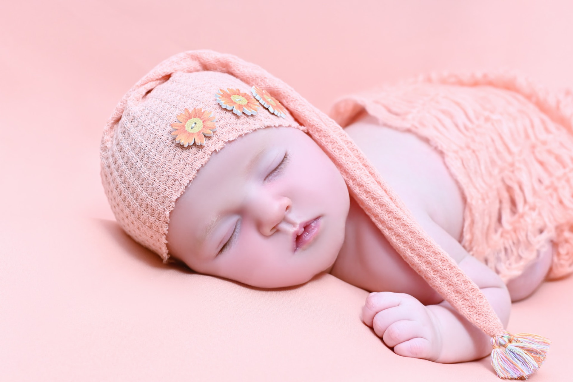 Bebé recién nacido dormido con gorrito de punto rosa sobre fondo coral en una sesión newborn en Madrid