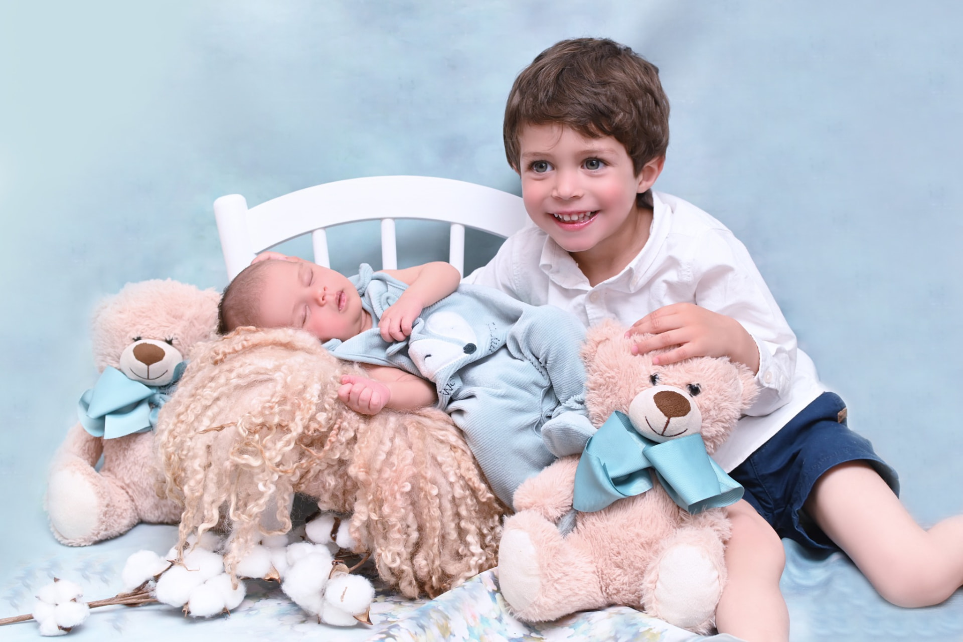 Hermano mayor sonriendo junto a su hermano recién nacido dormido entre ositos de peluche