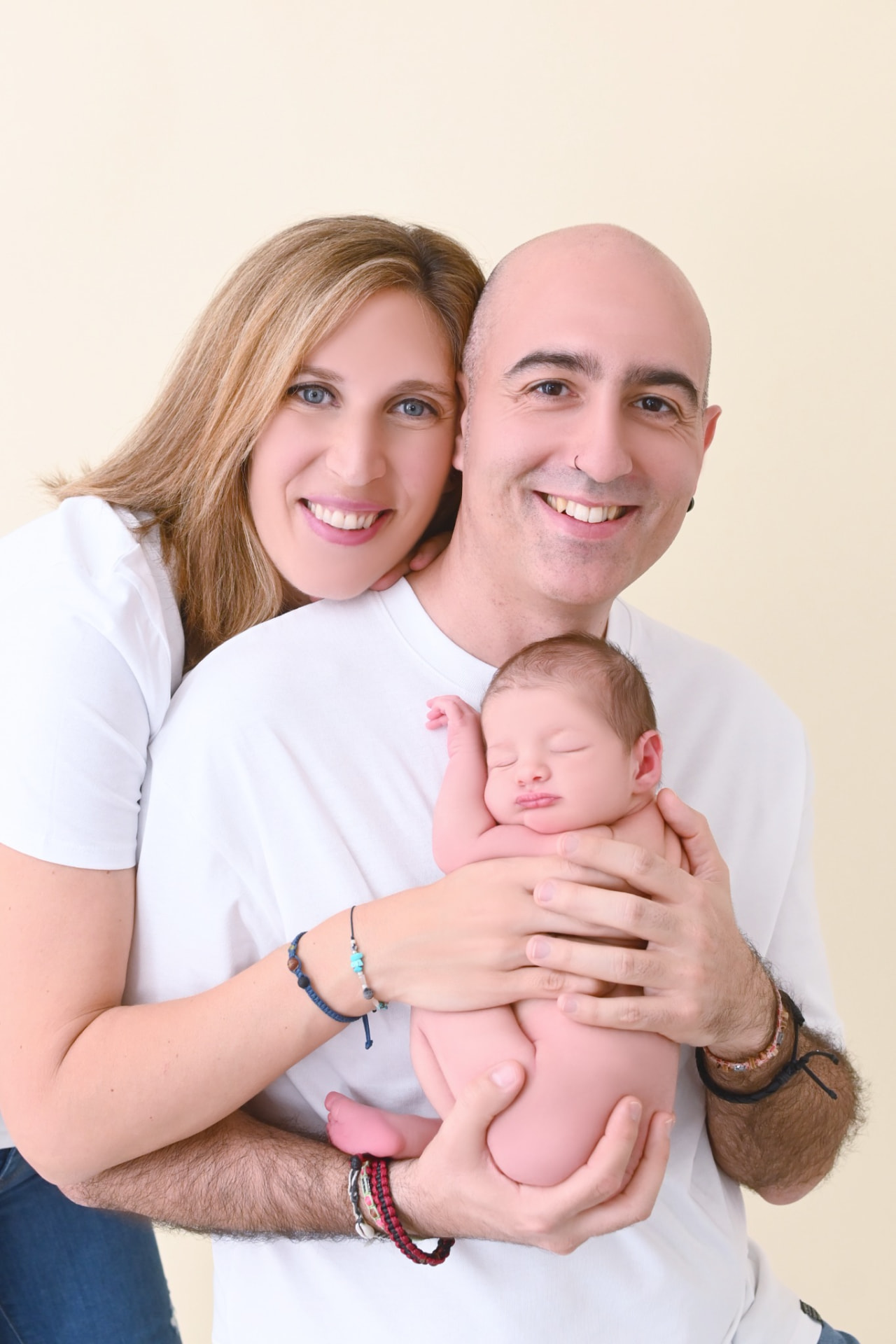 Padre y madre sonriendo a cámara mientras sostienen a su bebé recién nacido dormido en brazos